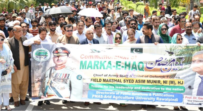 Students and faculty at PMAS‑AAUR participating in a commemorative walk, holding flags and banners in tribute to Pakistan’s armed forces.